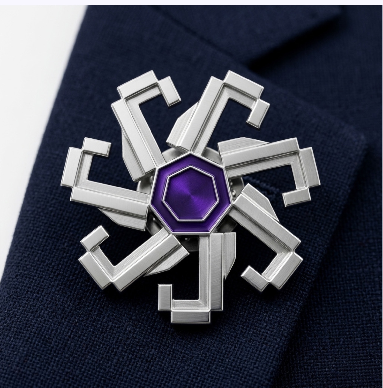 The Cycle Mark machined as a silver lapel badge with a faceted violet nucleus, worn on a navy suit.