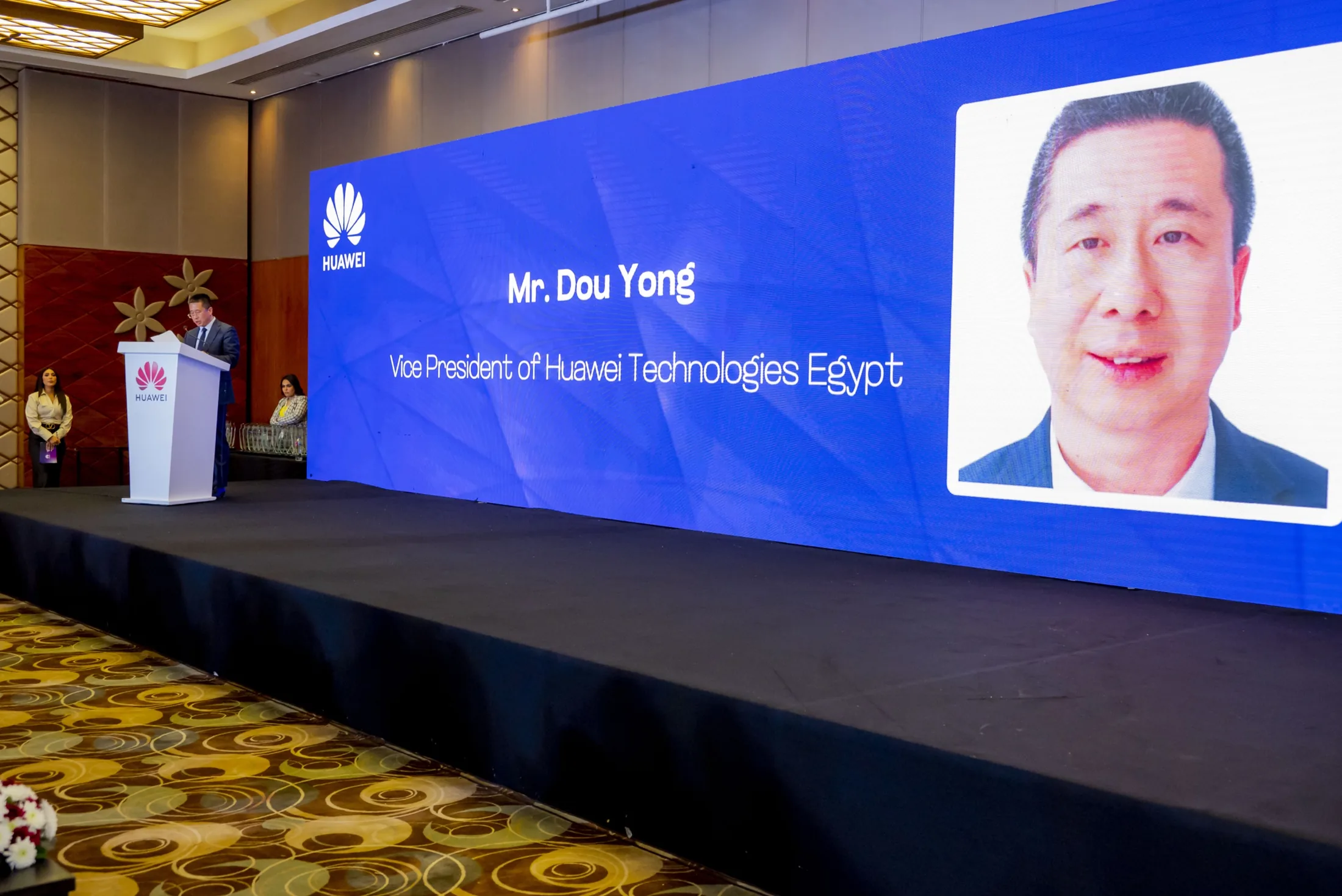 Mr. Dou Yong at the Huawei podium, his portrait and title on the keynote LED
