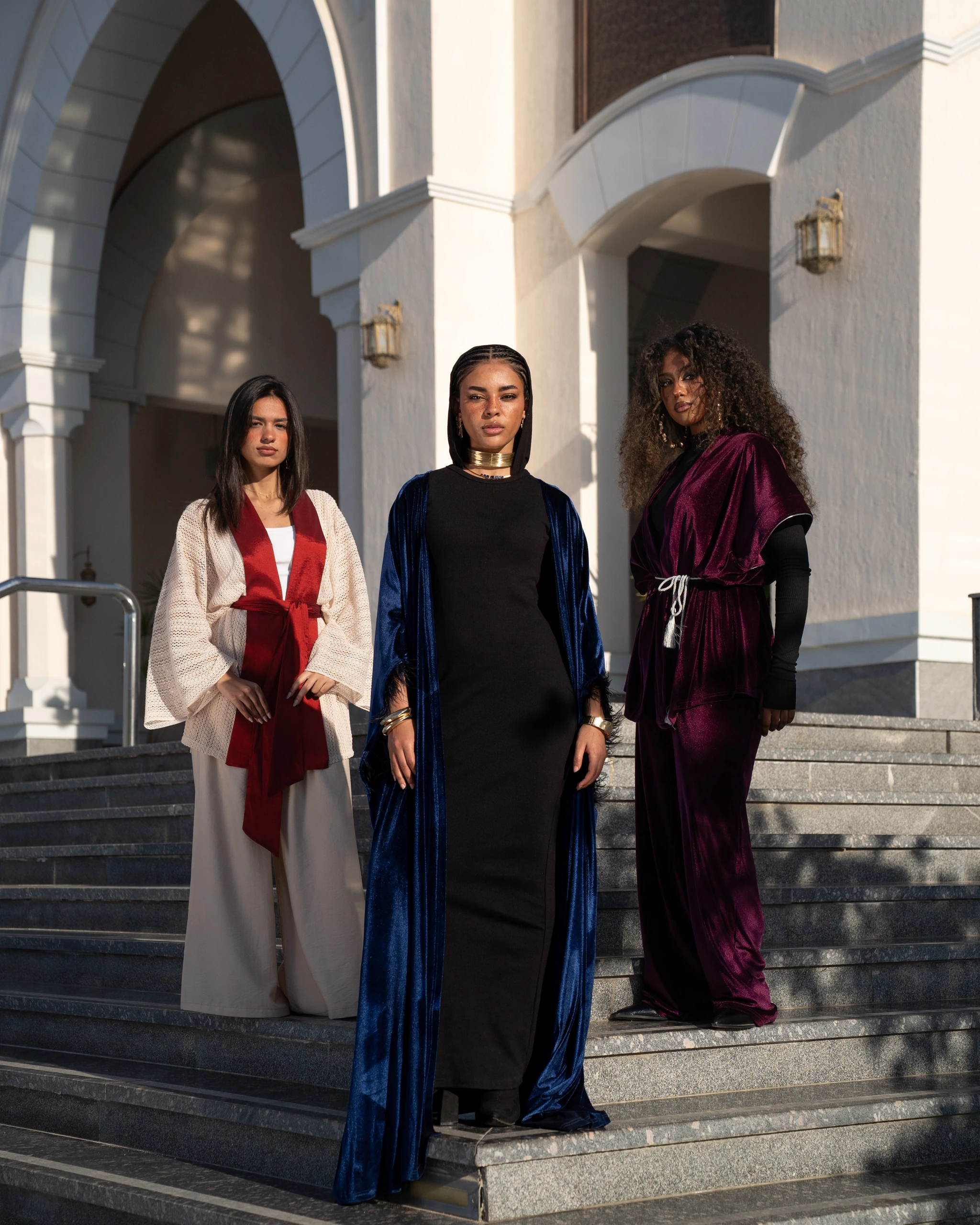 Khawia — three looks on the white mosque steps: cream, navy velvet and wine