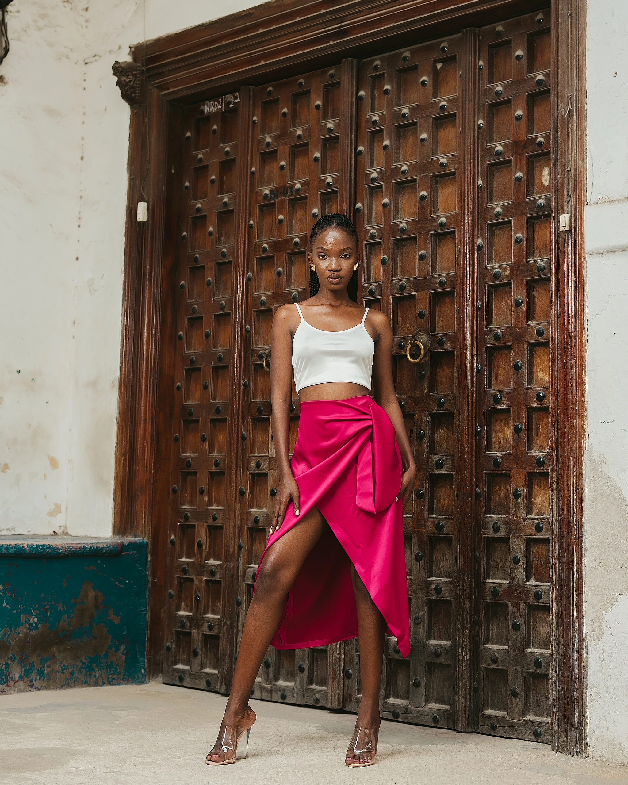 Khokha — an ivory bustier and magenta wrap skirt at a carved door, Zanzibar